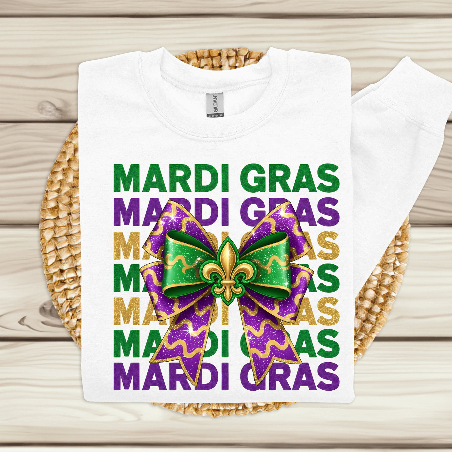 White t-shirt with Mardi Gras-themed design featuring a bow and text on a wooden surface.