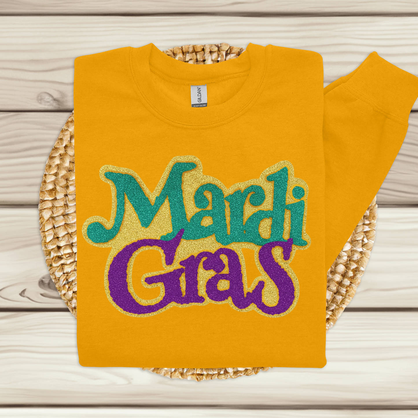 Yellow sweatshirt with 'Mardi Gras' text in green and purple on a woven mat.