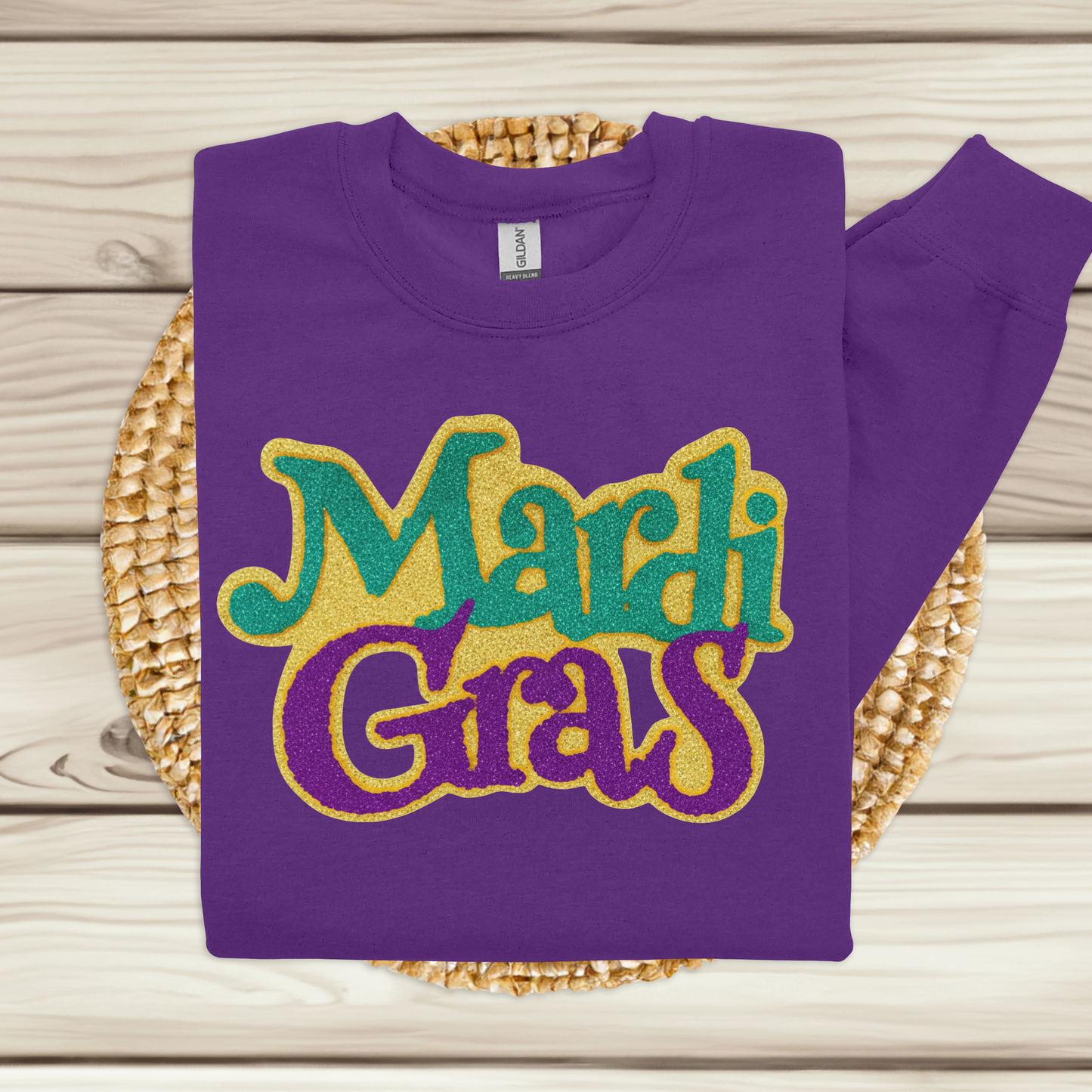 Purple sweatshirt with 'Mardi Gras' text in gold, green, and purple on a woven mat.