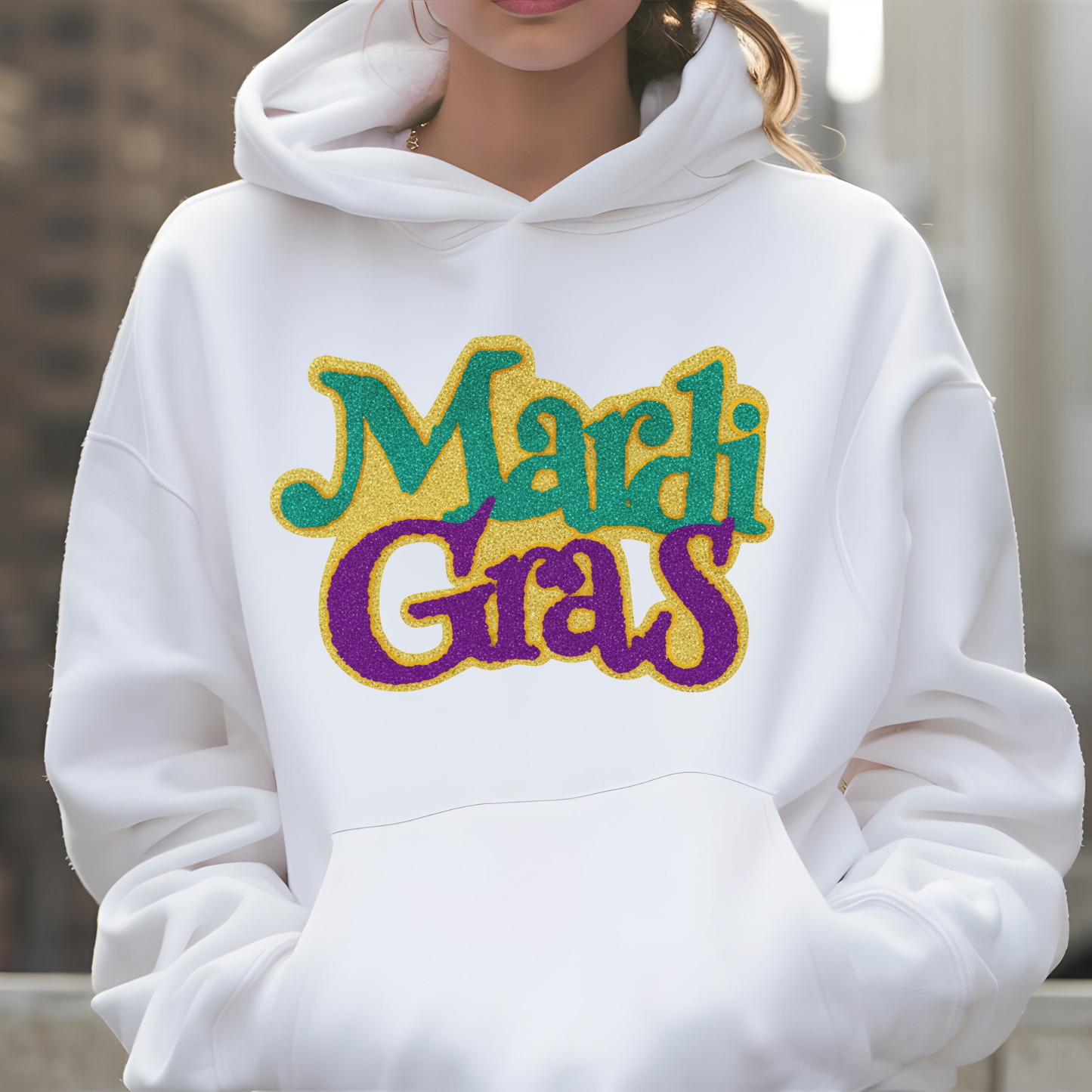 White hoodie with 'Mardi Gras' text in colorful letters on a blurred background