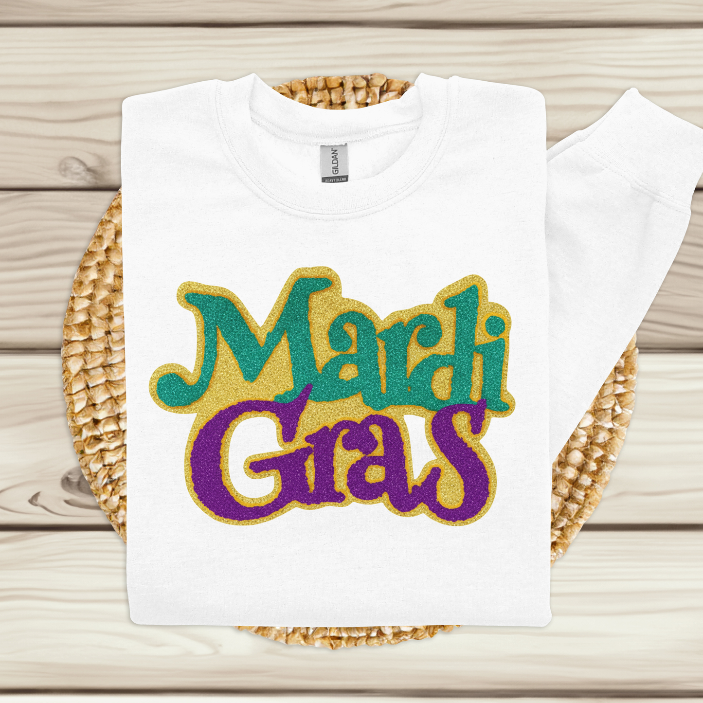 White t-shirt with 'Mardi Gras' text in colorful letters on a woven mat.