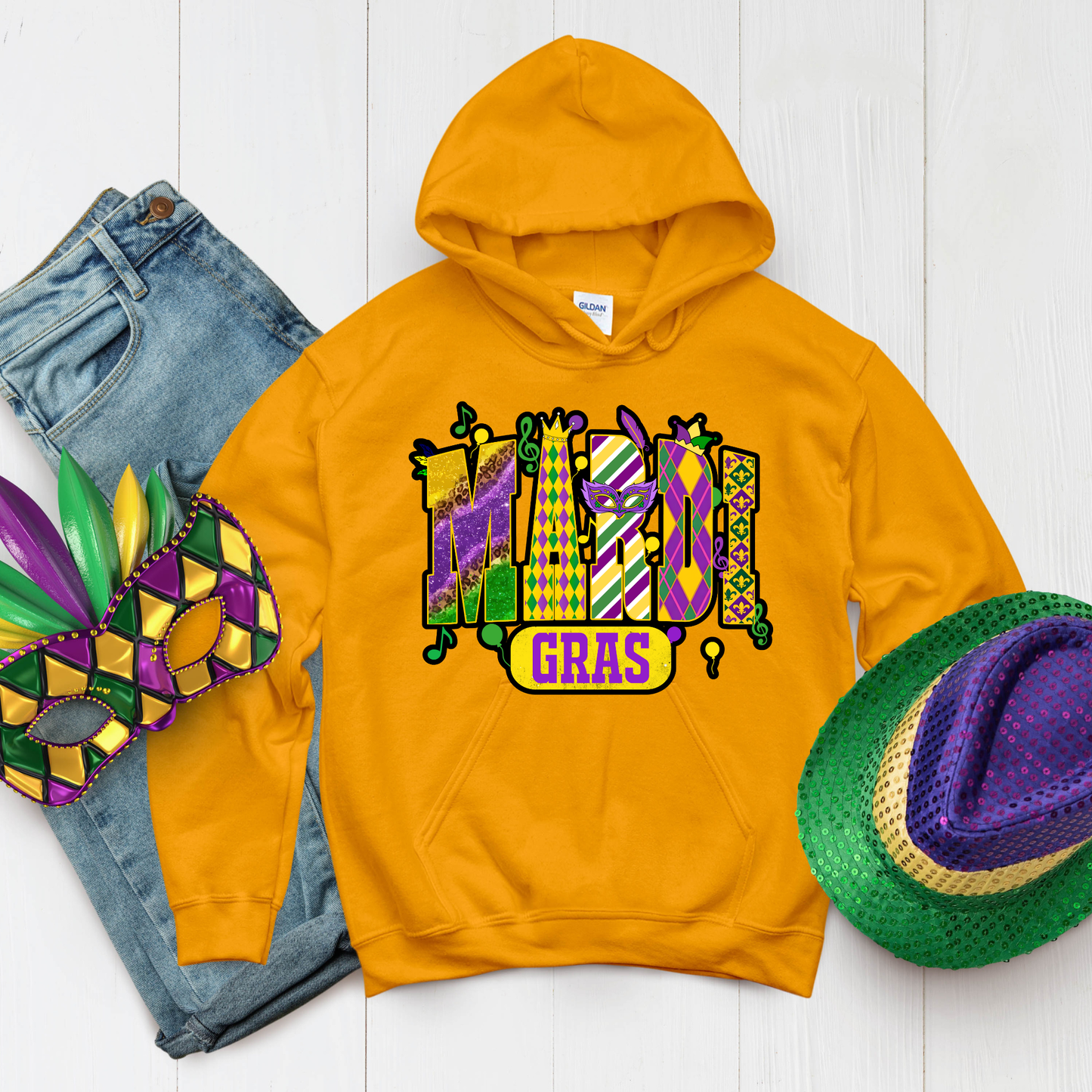 Yellow hoodie with Mardi Gras design, jeans, mask, and hat on a white background