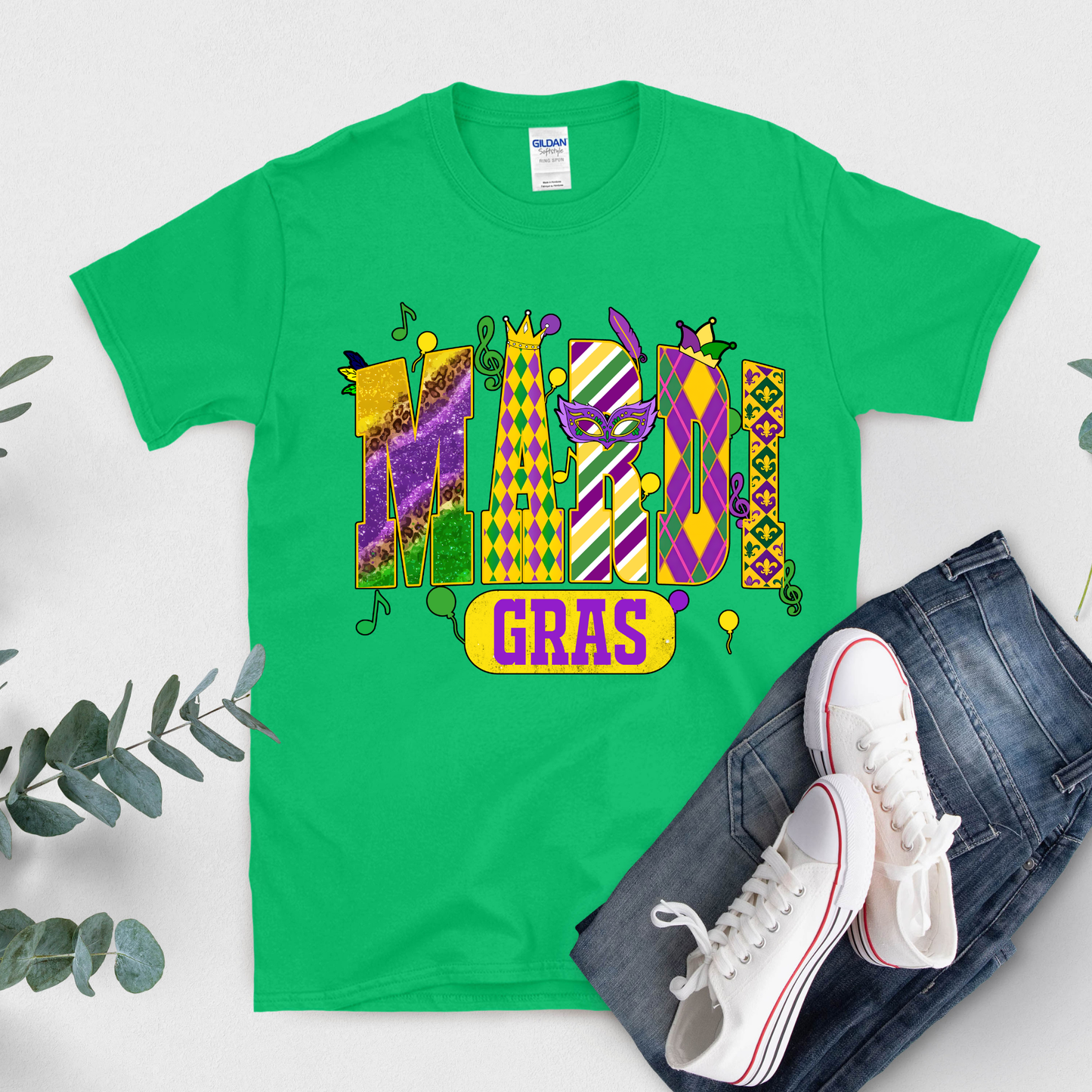 Green t-shirt with Mardi Gras design, white sneakers, and jeans on a light gray background