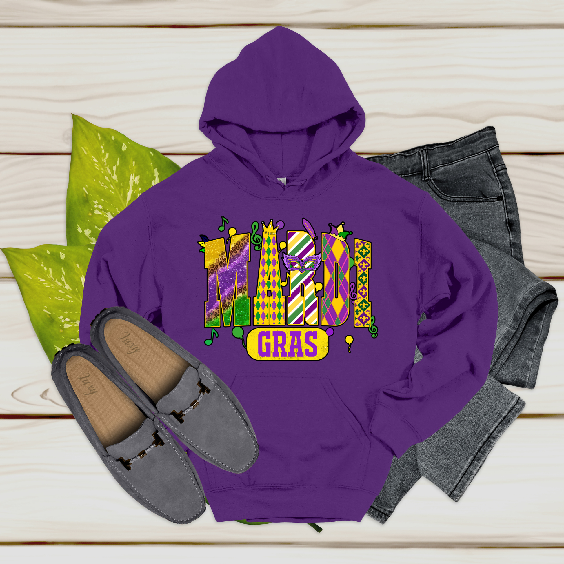 Purple hoodie with 'Mardi Gras' text, gray loafers, and jeans on a wooden surface