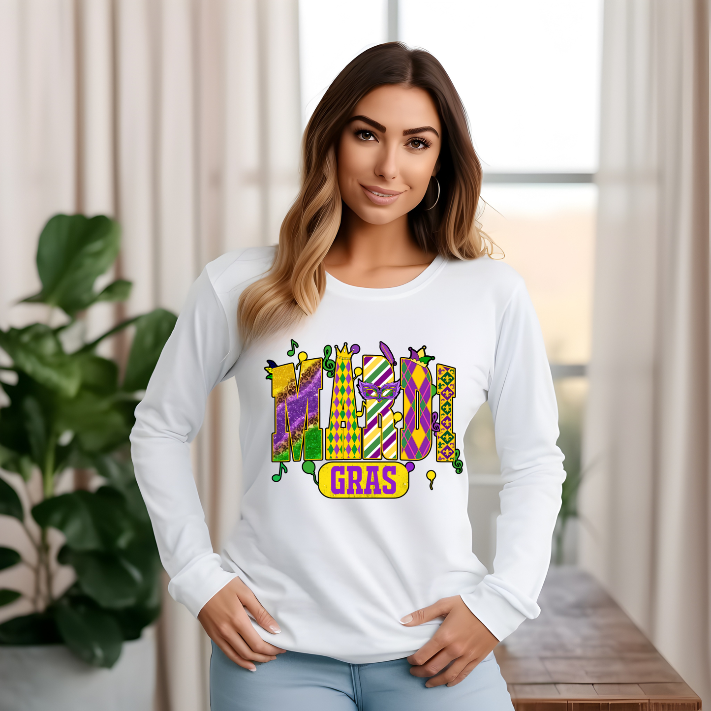 Woman wearing a white long-sleeve shirt with Mardi Gras design in a room with plants and a window.