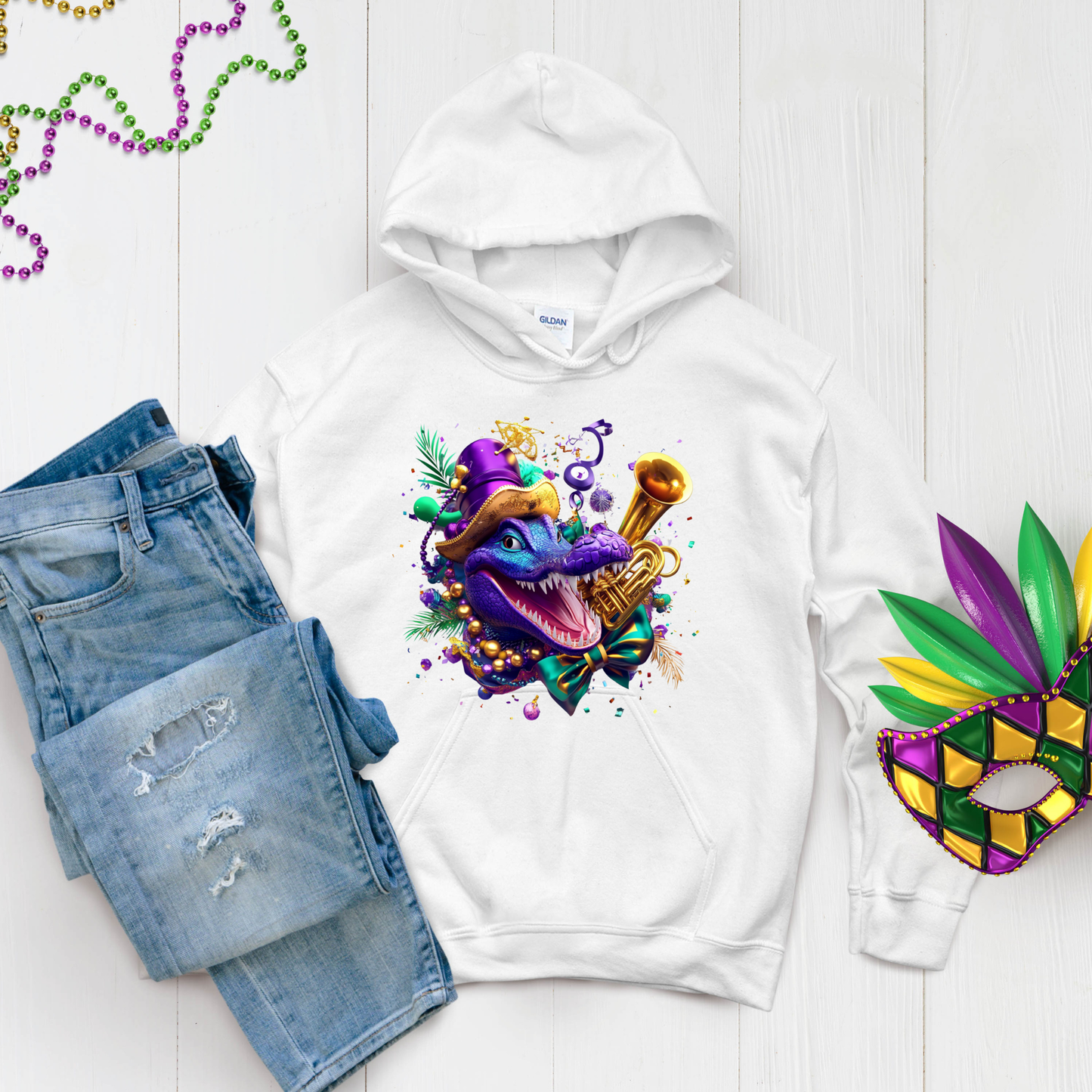 White hoodie with a colorful Mardi Gras-themed design, paired with denim shorts and a mask on a light wooden surface.