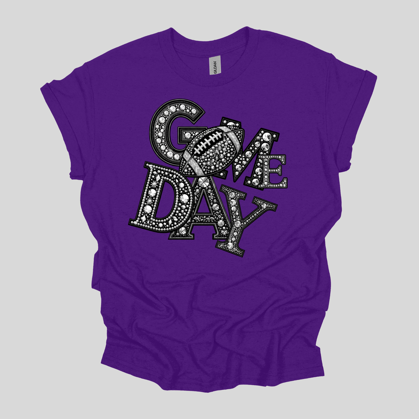 A purple short-sleeve t-shirt with a graphic reading 'COME DAY' in black and white, styled with a football motif, laid flat on a light gray background.