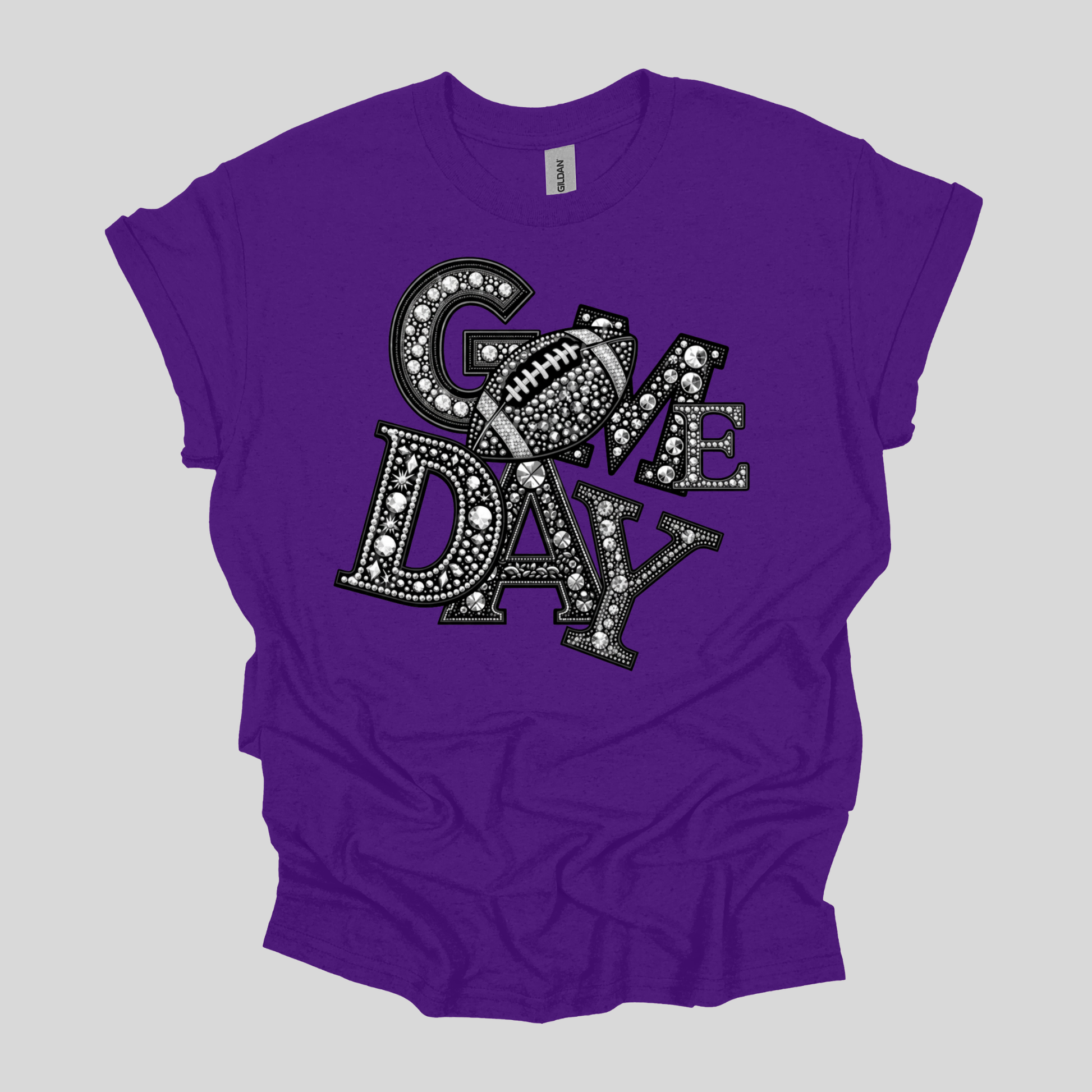 A purple short-sleeve t-shirt with a graphic reading 'COME DAY' in black and white, styled with a football motif, laid flat on a light gray background.