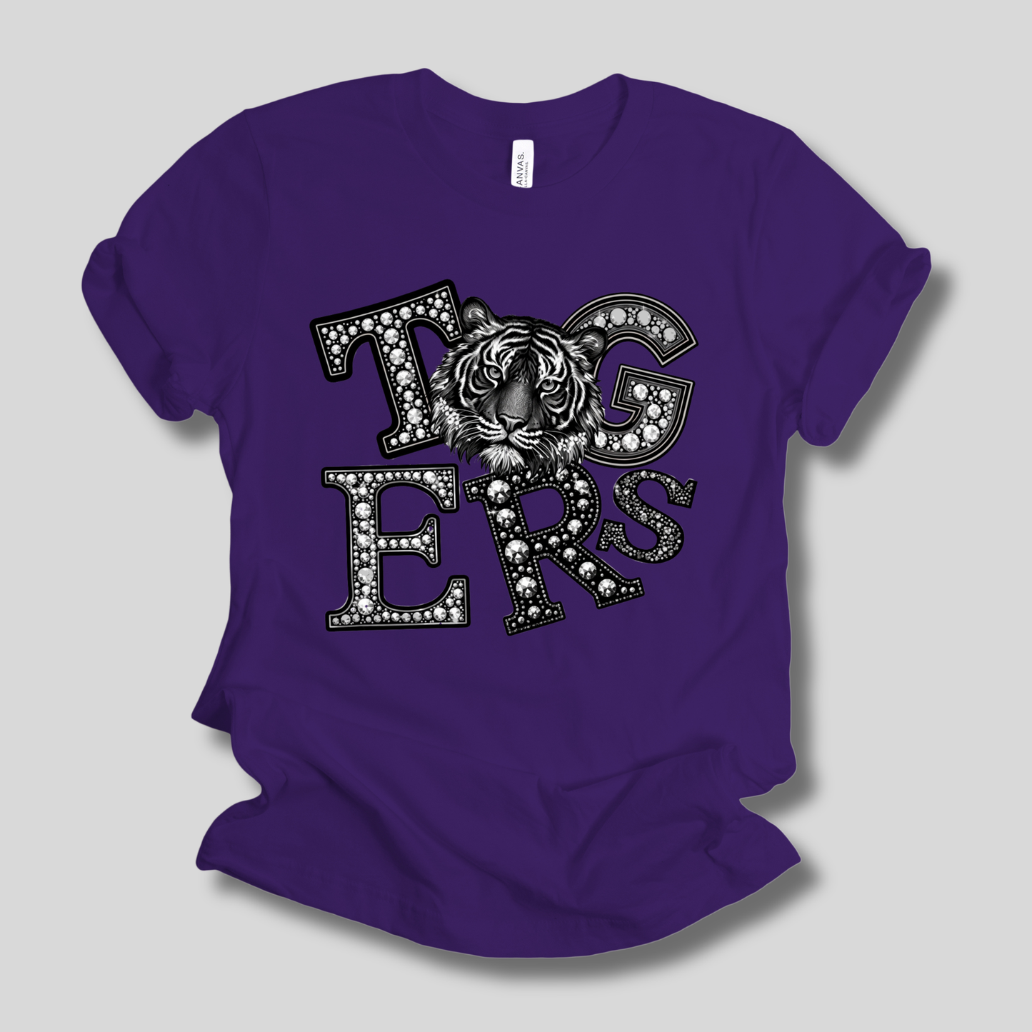A purple short-sleeve t-shirt with a black and white graphic reading 'TIGERS' featuring a tiger face design, shown on a neutral gray background.