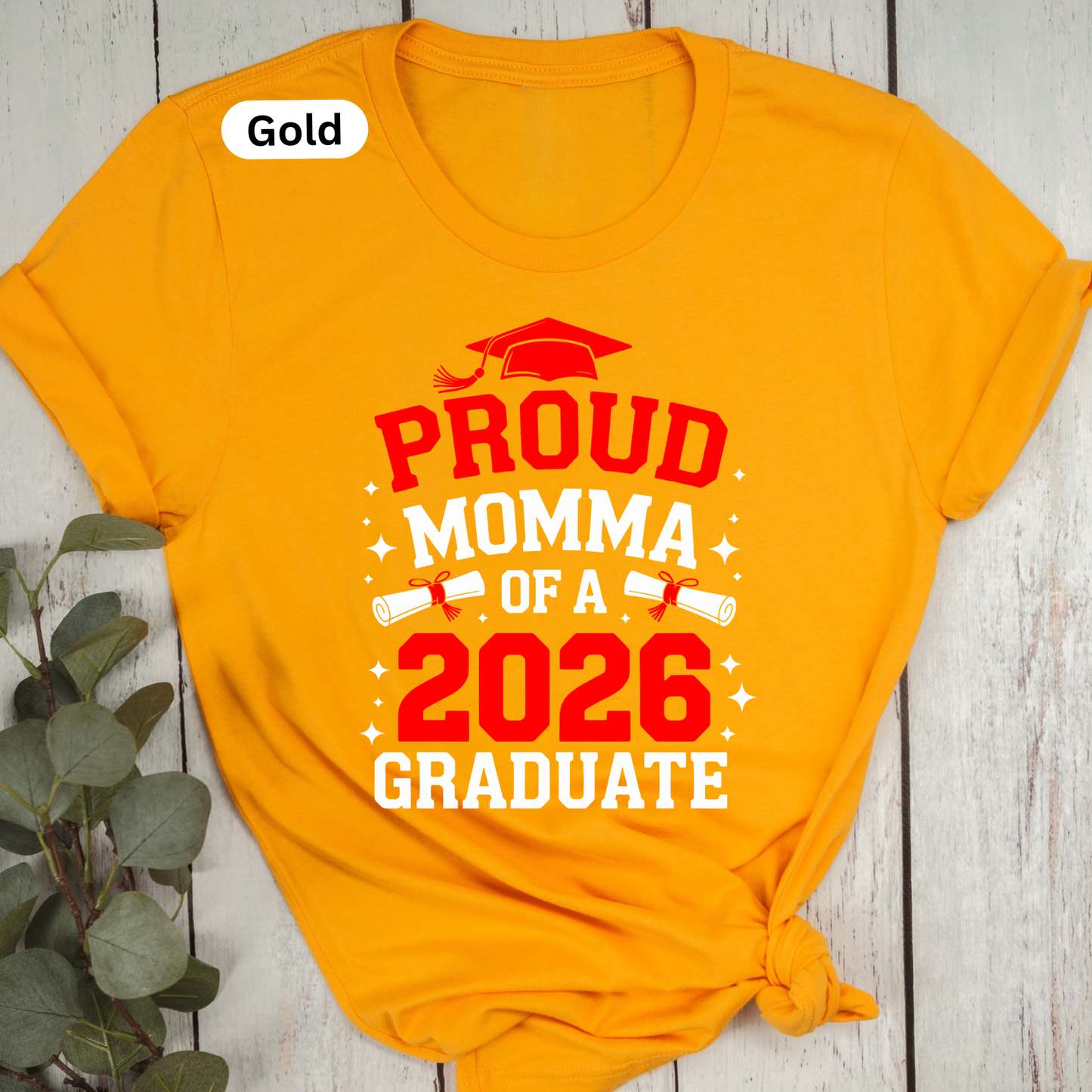 Yellow t-shirt with 'Proud Momma of a 2026 Graduate' text on a wooden surface.