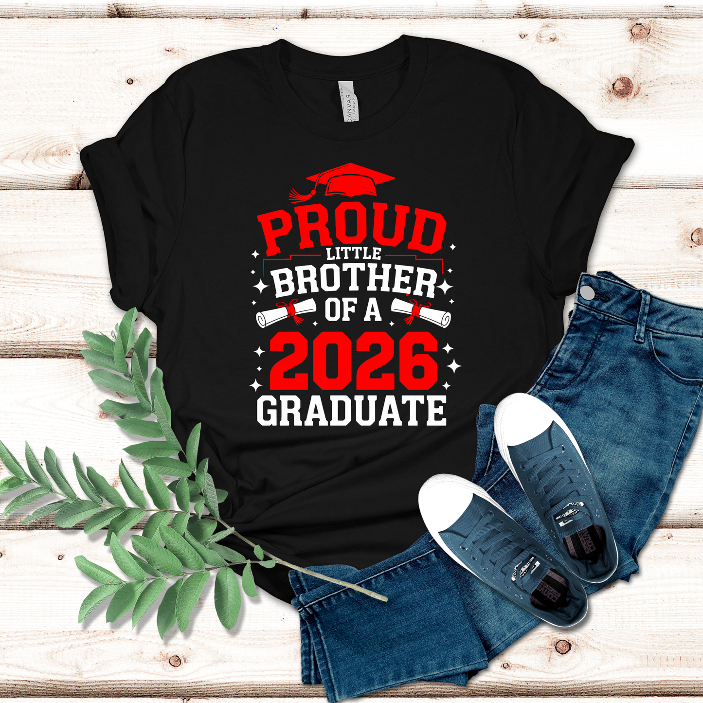 Black t-shirt with 'Proud Little Brother of a 2026 Graduate' text on a wooden surface with jeans and shoes.