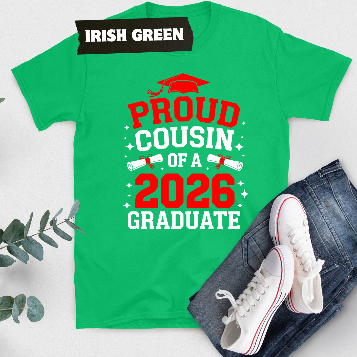 Green t-shirt with 'Proud Cousin of a 2026 Graduate' text, white sneakers, and jeans on a light gray background.