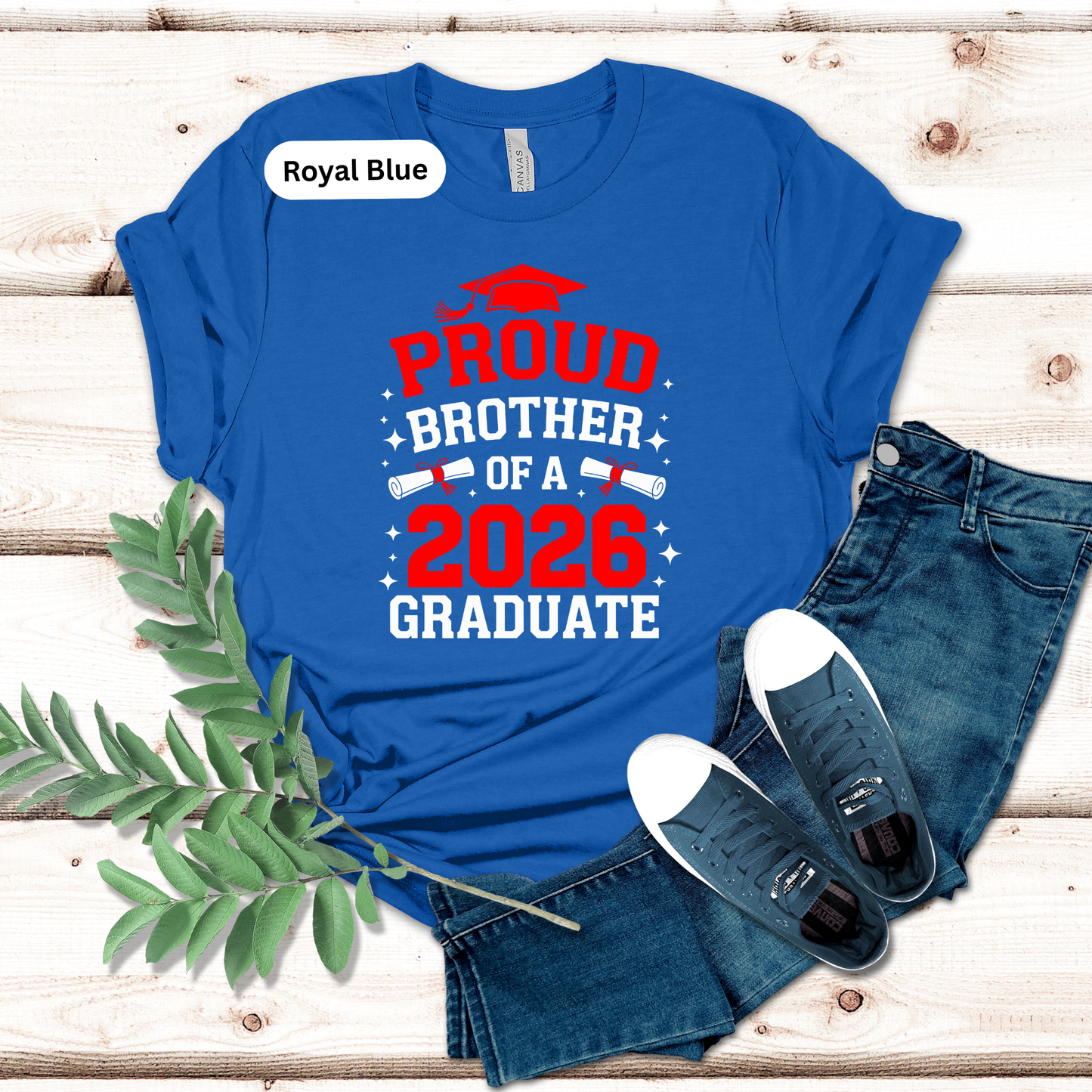 Blue t-shirt with 'Proud Brother of a 2026 Graduate' text on a wooden surface with jeans and sneakers.