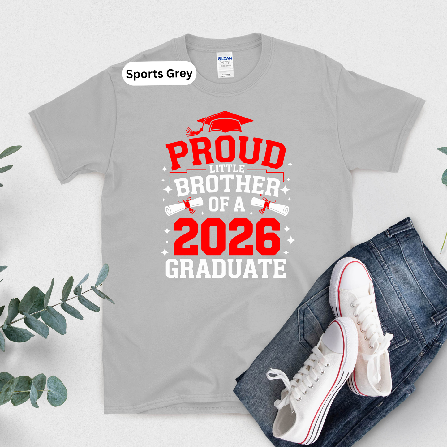 Gray t-shirt with 'Proud Little Brother of a 2026 Graduate' text, white sneakers, and jeans on a light background.
