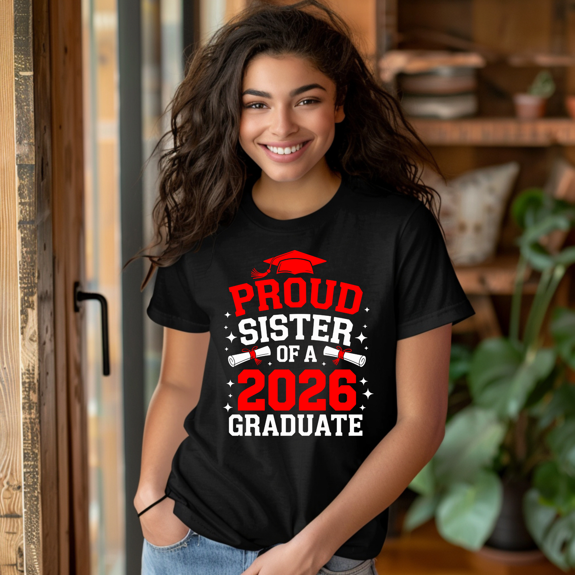 Woman wearing a black t-shirt with 'Proud Sister of a 2026 Graduate' text, standing indoors.