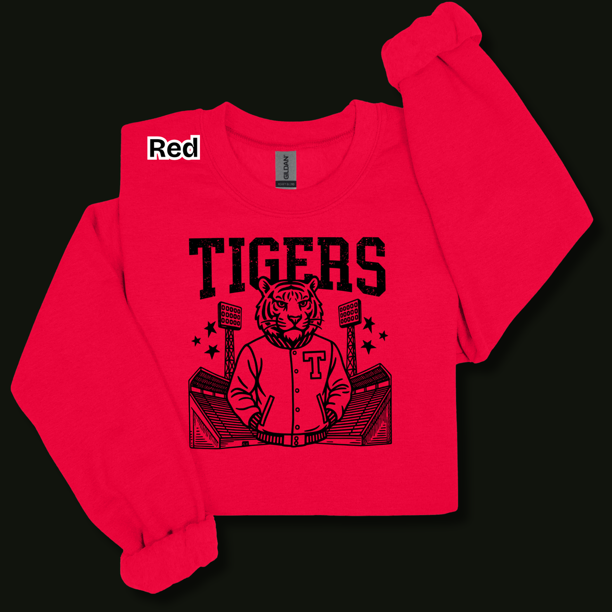 A bright red long-sleeve sweatshirt with a black graphic of a tiger mascot in a baseball jersey and the word 'TIGERS' on the front, displayed on a solid black background. A small white label with 'Red' is visible near the collar.