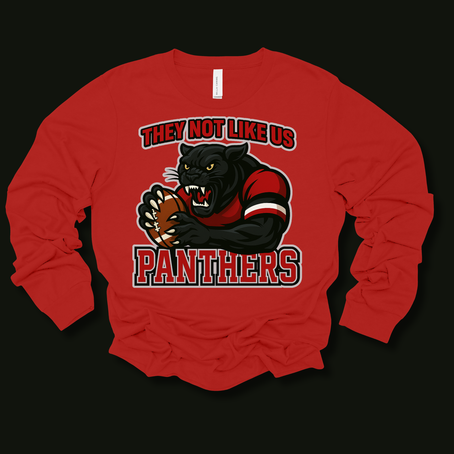 A red long-sleeve t-shirt with a graphic of a black panther holding a football, with the text 'THEY NOT LIKE US PANTHERS' in red and black. The shirt is laid flat on a black background.