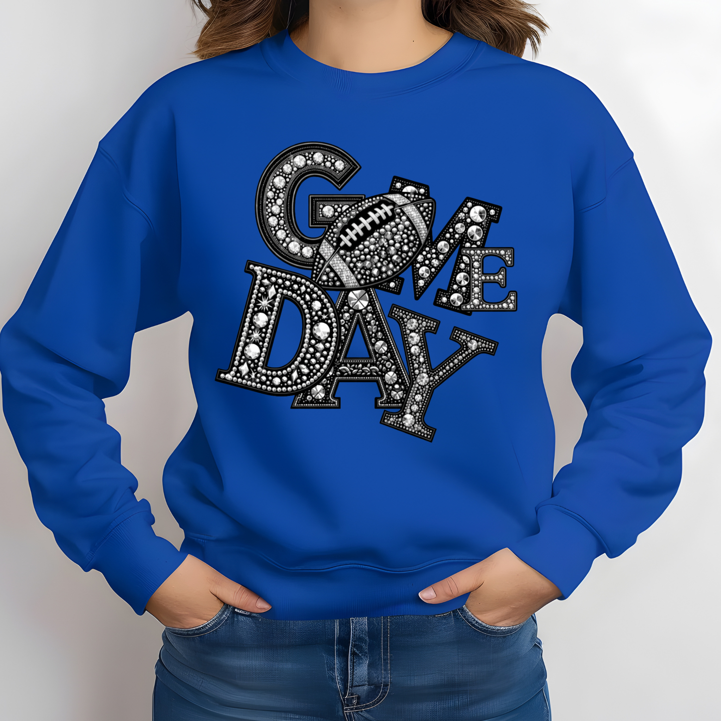 A person wearing a royal blue crewneck sweatshirt with a large 'COME DAY' football graphic on the chest, paired with blue jeans, against a plain light gray background.