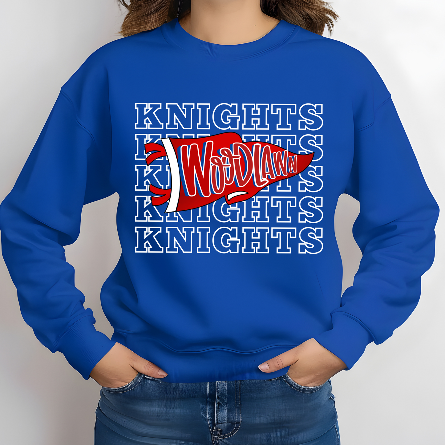 A person wearing a royal blue crewneck sweatshirt with a red and white 'Woodlawn' sports graphic over a repeating white 'KNIGHTS' text pattern, paired with blue jeans against a light gray background.