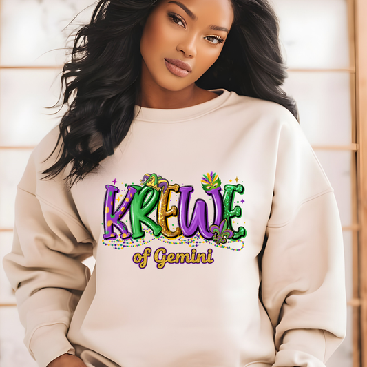 Woman wearing a beige sweatshirt with 'Krewe of Gemini' text in colorful letters.