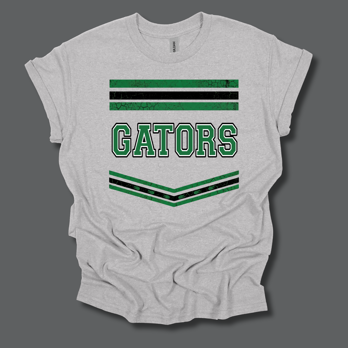 A light heather gray t-shirt with a distressed green and black graphic featuring the word 'GATORS' and decorative stripes, displayed on a dark gray background.