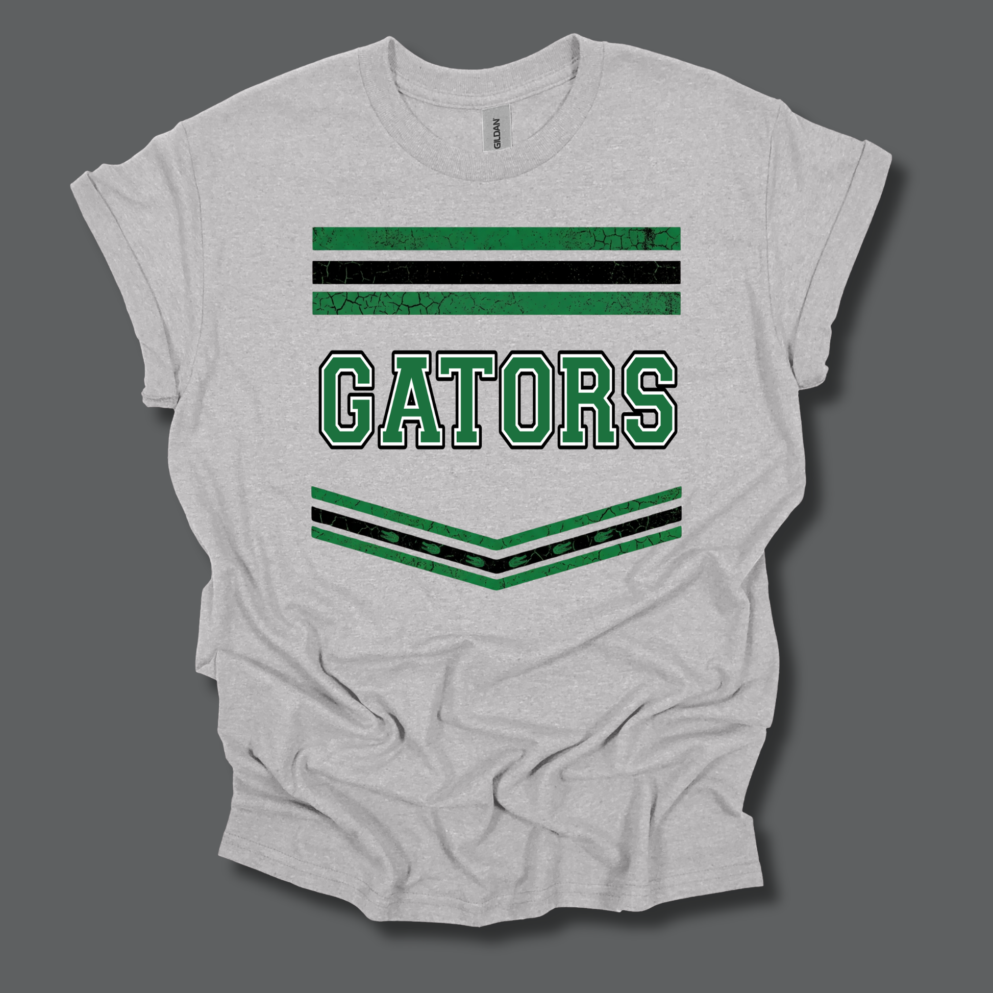 A light heather gray t-shirt with a distressed green and black graphic featuring the word 'GATORS' and decorative stripes, displayed on a dark gray background.
