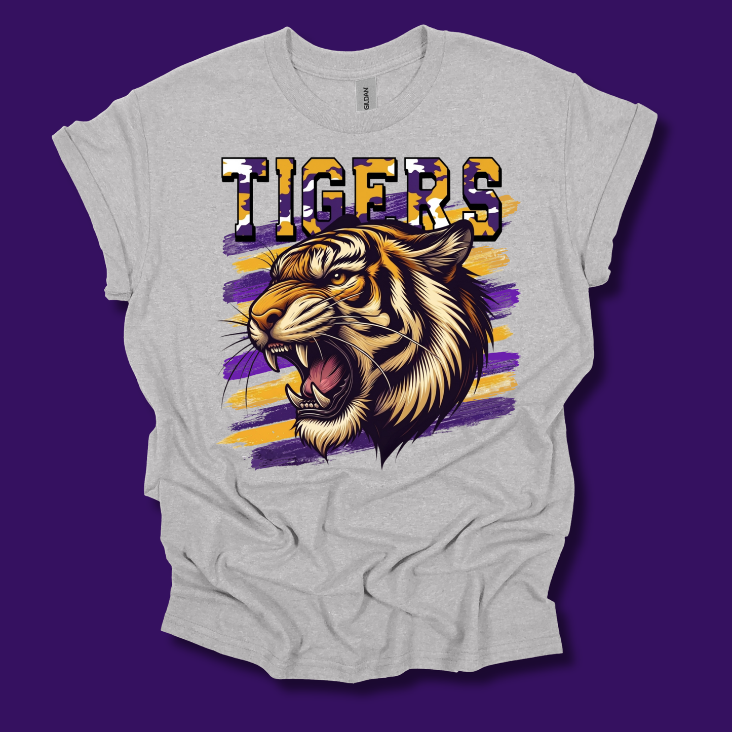 A light heather gray t-shirt featuring a graphic print of a roaring tiger and the word 'TIGERS' in a patterned font, set against a solid purple background.
