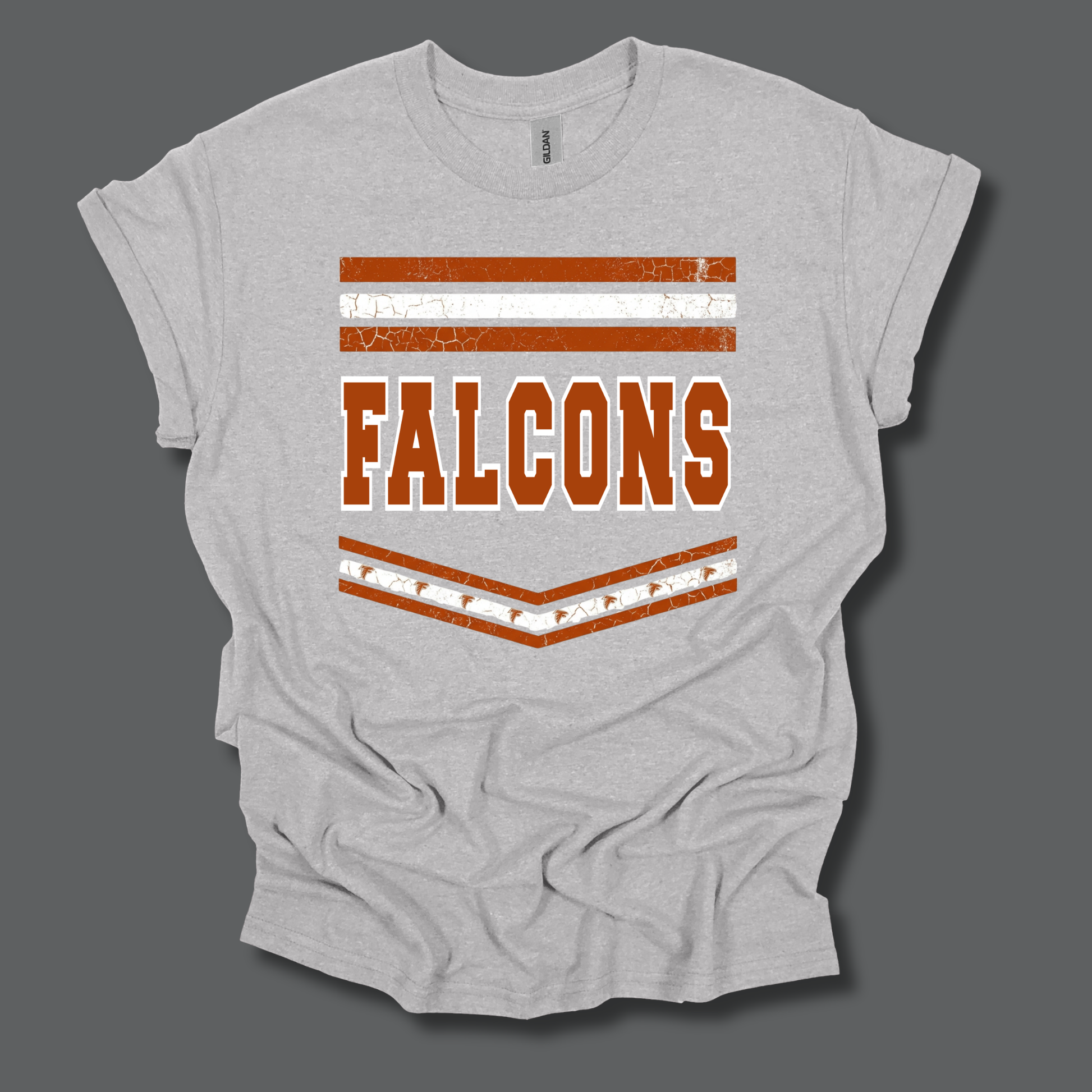 A light heather gray t-shirt with a distressed orange and white graphic featuring the word 'FALCONS' and horizontal stripes, displayed on a dark gray background.