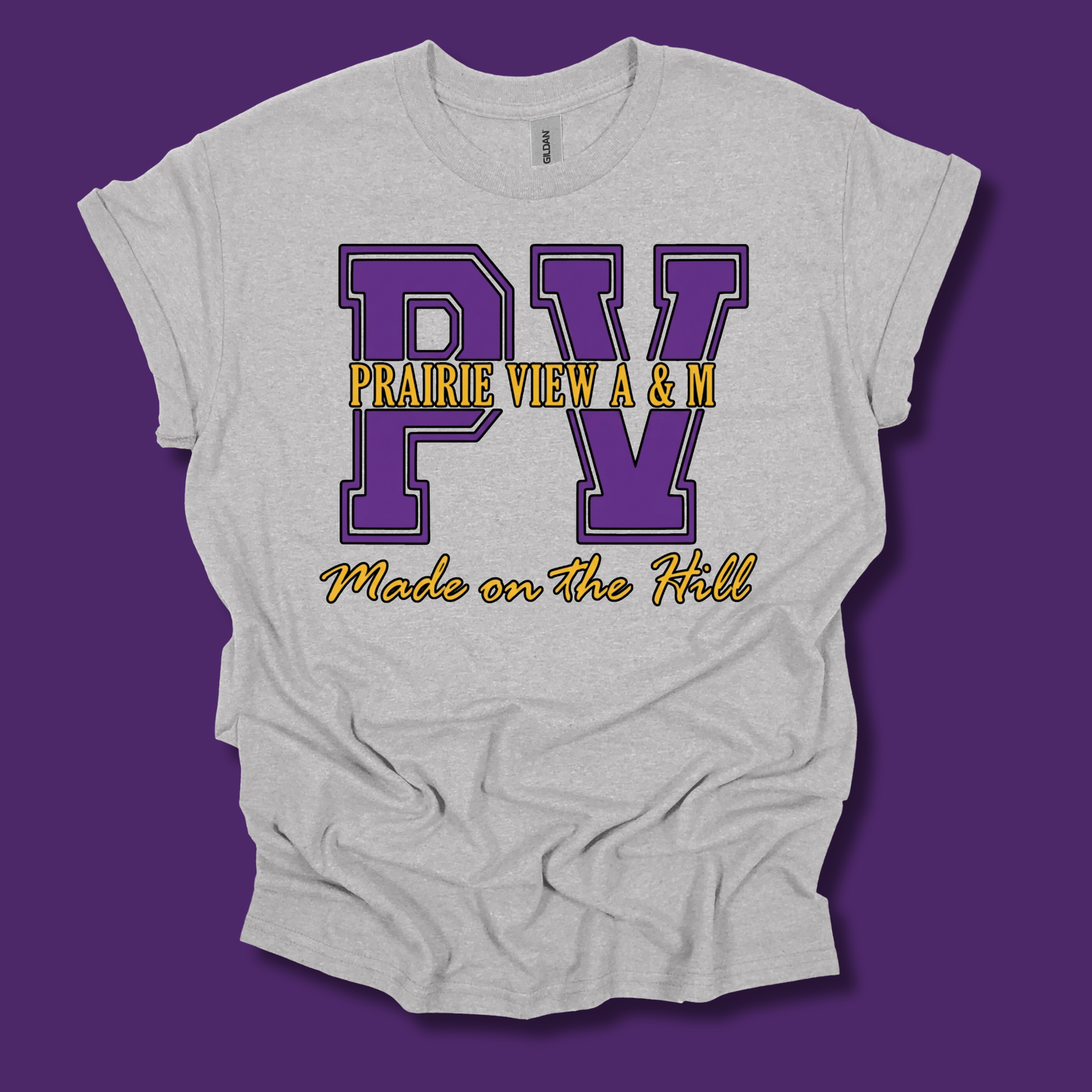 A light heather gray t-shirt with a graphic print featuring purple varsity-style letters 'PV' and yellow text reading 'PRAIRIE VIEW A & M' and 'Made on The Hill', shown on a solid purple background.
