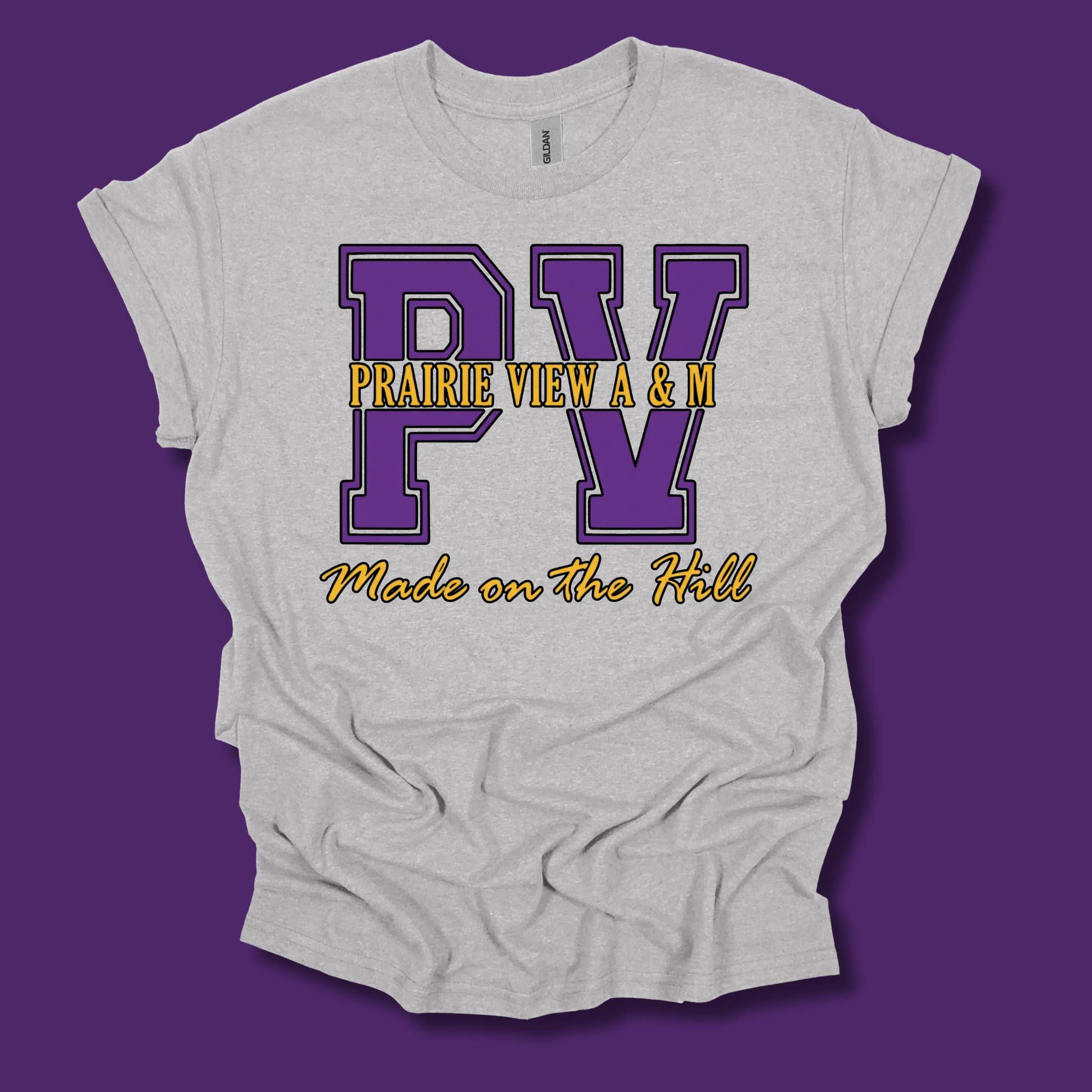 A light heather gray t-shirt with a graphic print featuring purple varsity-style letters 'PV' and yellow text reading 'PRAIRIE VIEW A & M' and 'Made on The Hill', shown on a solid purple background.