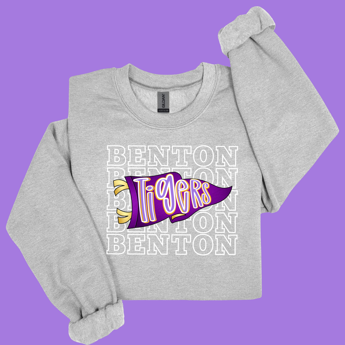 A light heather gray long-sleeve sweatshirt with a 'Benton Tigers' graphic on the front, displayed on a solid purple background.