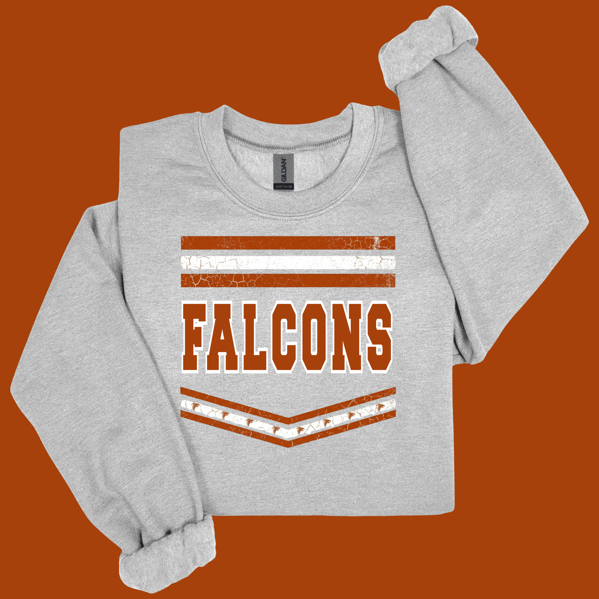 A light heather gray long-sleeve sweatshirt with a distressed orange and white graphic that reads 'FALCONS' on the front, displayed against a solid orange background.