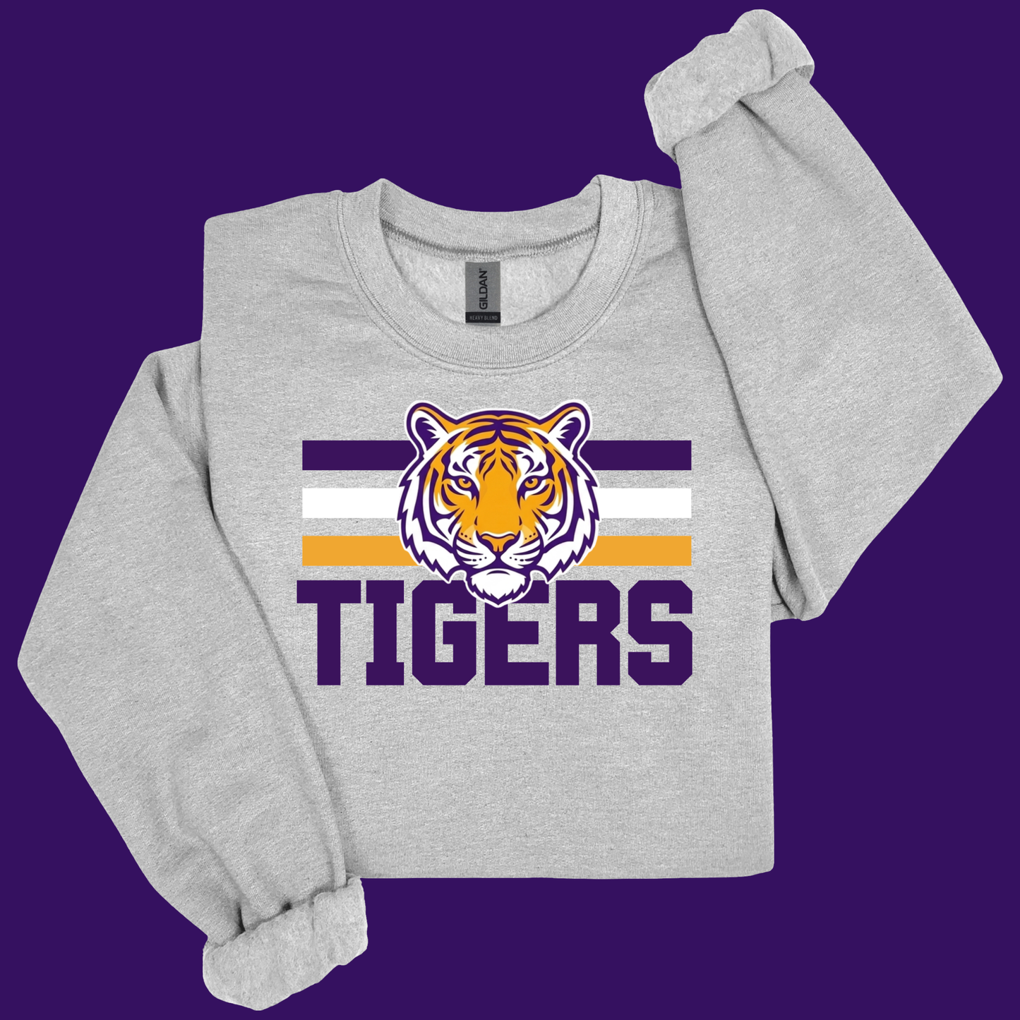A light heather gray crewneck sweatshirt featuring a purple, white, and orange tiger mascot graphic with the word 'TIGERS' underneath, displayed on a solid purple background.