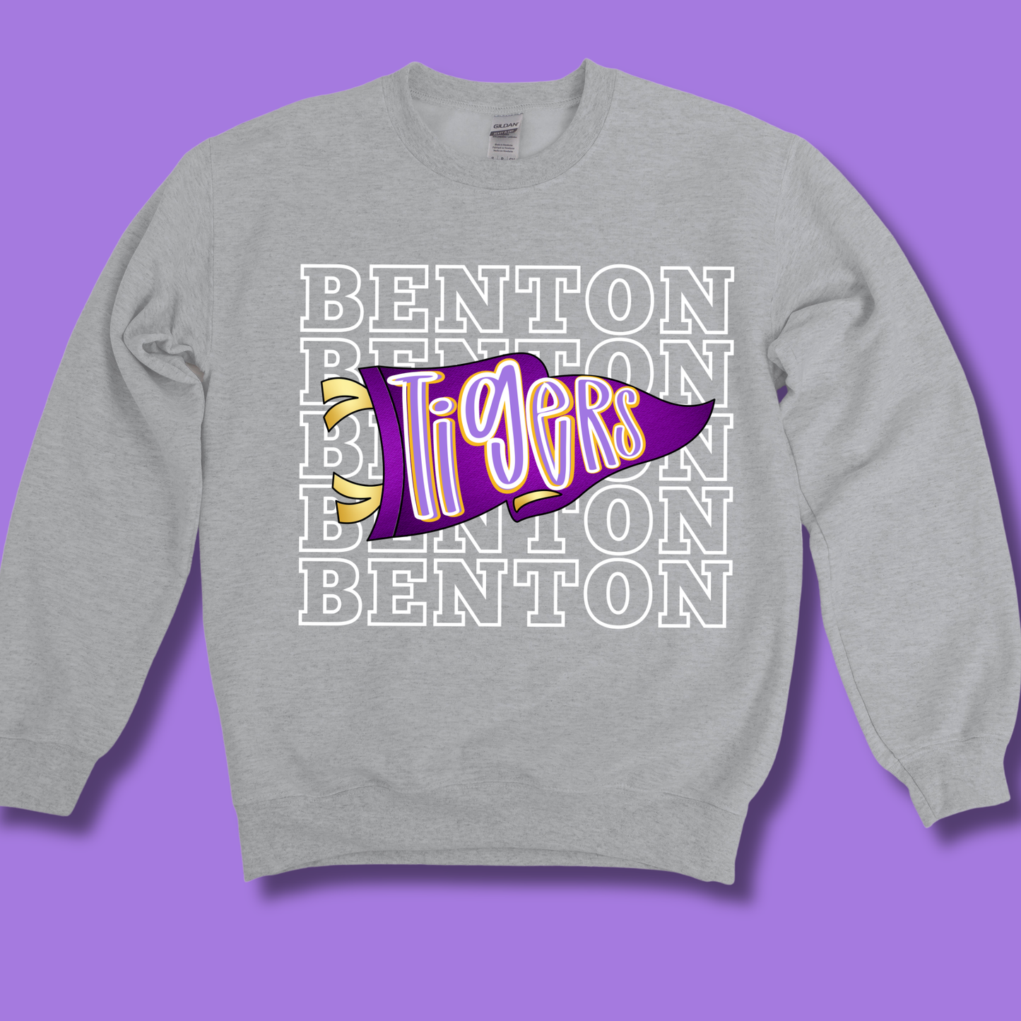 A heather gray crewneck sweatshirt featuring a purple and yellow 'Tigers' pennant graphic with 'BENTON' text, displayed on a solid purple background.
