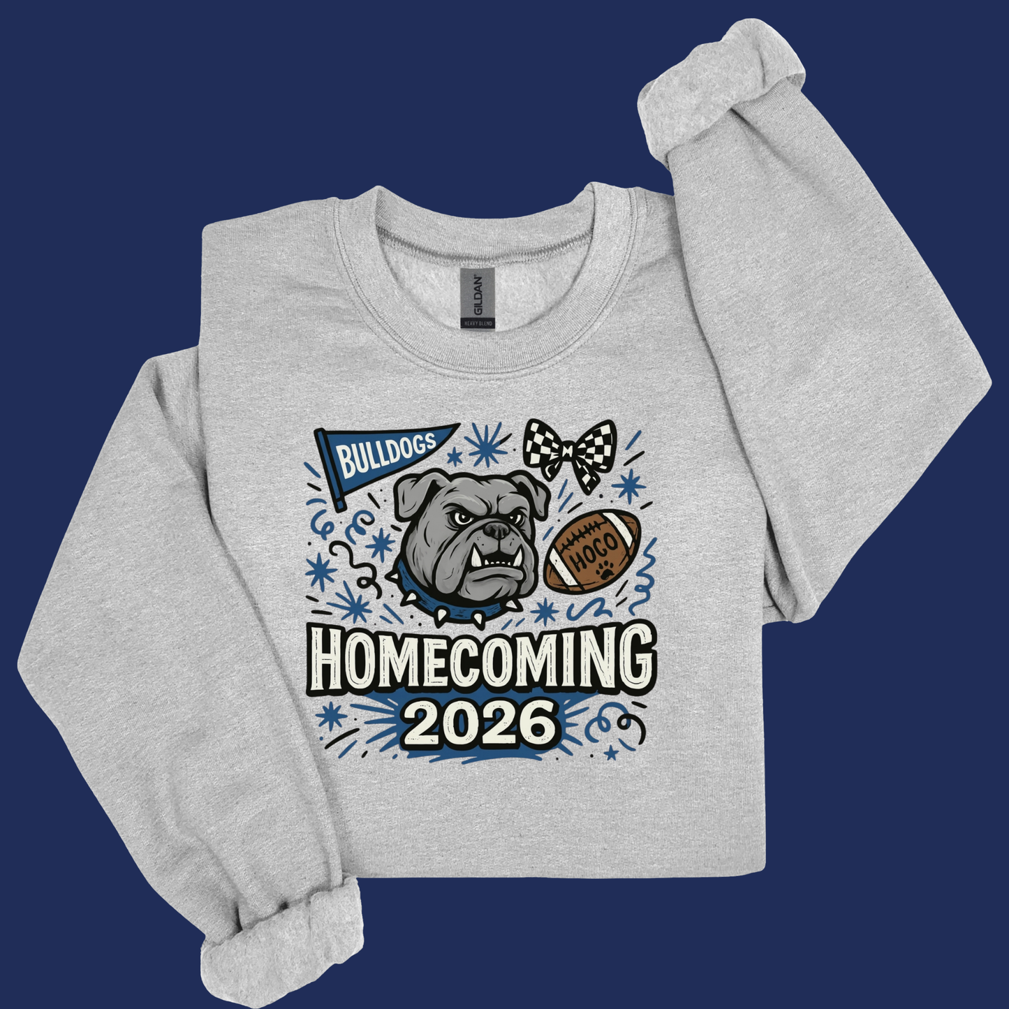 A light heather gray long-sleeve sweatshirt with a custom graphic print on the front. The graphic features a bulldog, a football, a bowtie, and the text 'BULLDOGS', 'HOMECOMING', and '2026' in blue, black, and white.