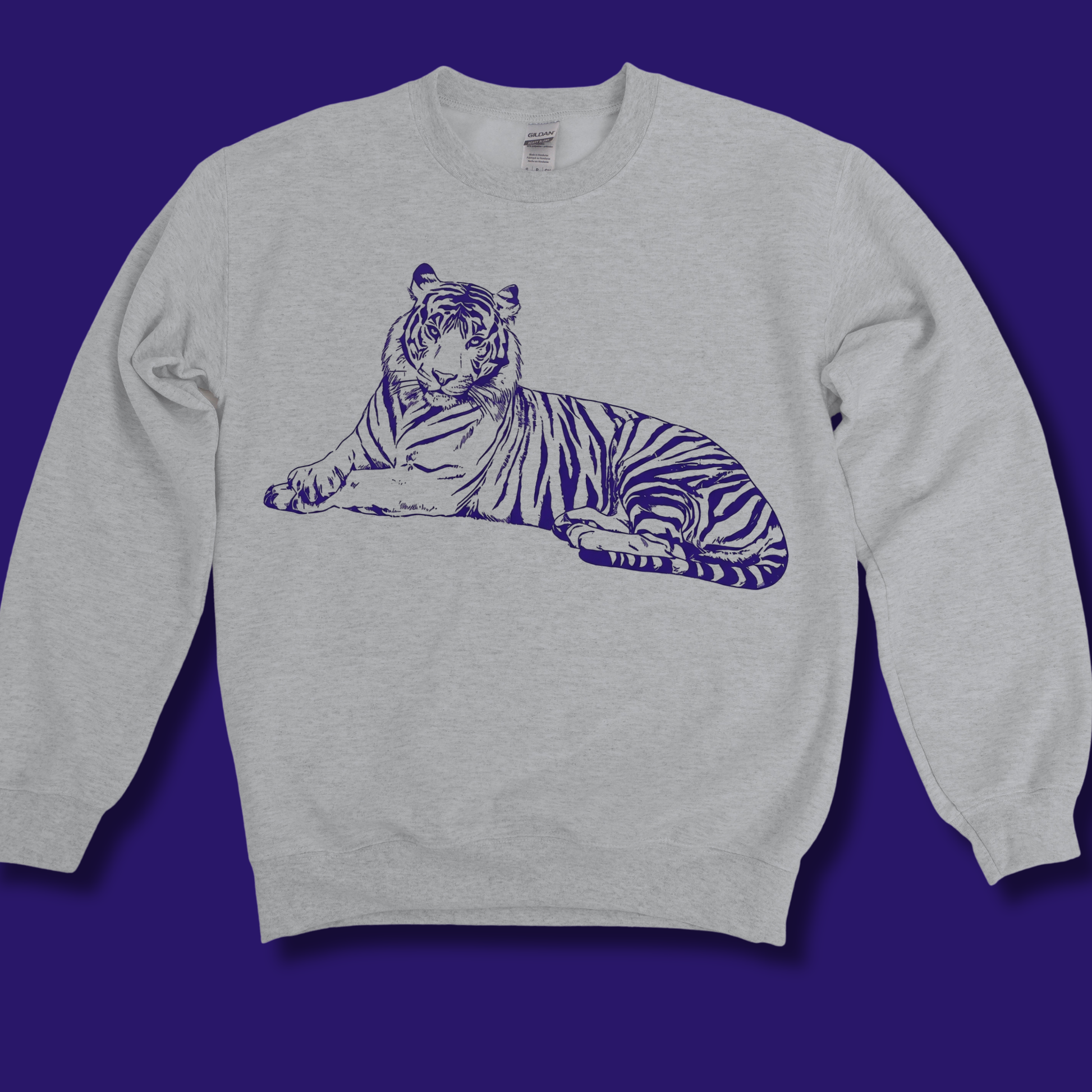 A light heather gray crewneck sweatshirt featuring a dark purple line art graphic of a lying tiger on the chest, displayed against a solid dark purple background.