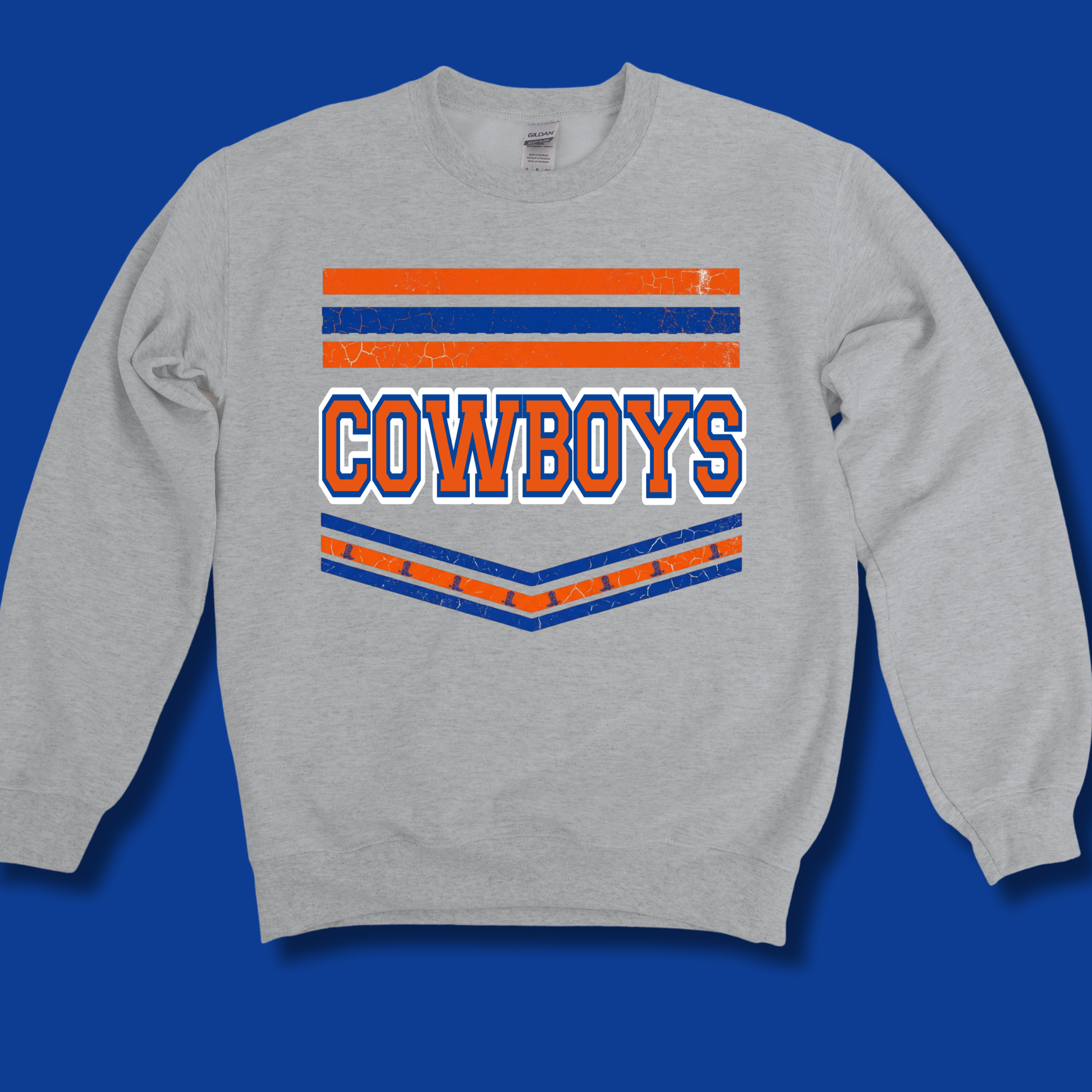 A light heather gray crewneck sweatshirt featuring a distressed orange and blue graphic with the word 'COWBOYS' in white outlined letters, displayed against a solid blue background.