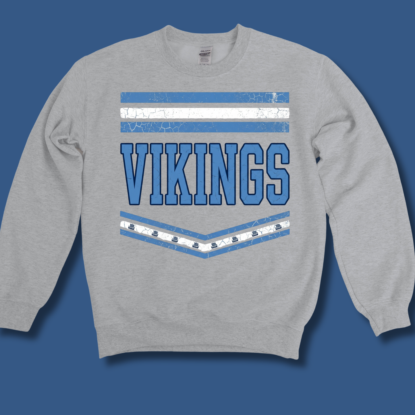 A heather gray crewneck sweatshirt featuring a distressed blue and white graphic with the word 'VIKINGS' and horizontal stripes, displayed on a solid blue background.