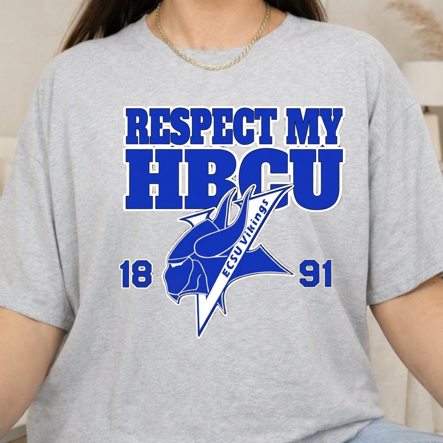 A person wearing a heather gray short-sleeve t-shirt with a blue graphic print that reads 'RESPECT MY HBCU' and '1891' with a blue mascot logo. The photo is cropped from the neck down, showing the torso and arms.