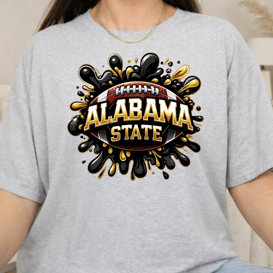 A person wearing a light heather gray t-shirt with a large graphic print on the front. The graphic features a football with the words 'ALABAMA STATE' in bold gold letters, surrounded by black and gold paint splatters.