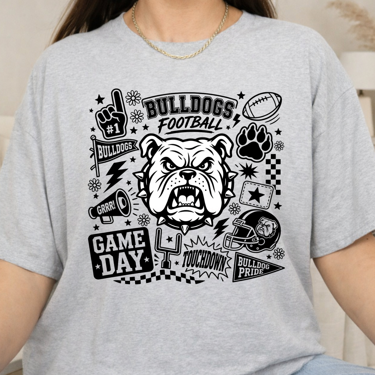 A woman wearing a light heather gray t-shirt with a black graphic print featuring an angry bulldog, football, paw print, and the words 'BULLDOGS FOOTBALL' and 'GAME DAY'.