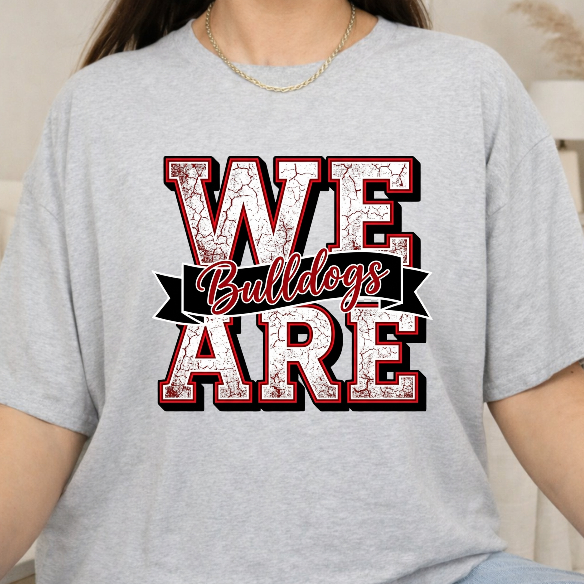 A person wearing a light heather gray t-shirt with a graphic that reads 'WE Bulldogs ARE' in distressed red, white, and black lettering.