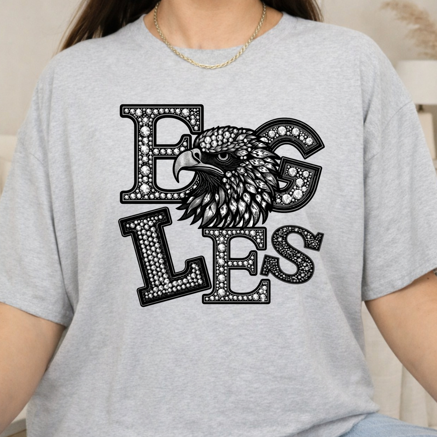 A person wearing a light heather gray t-shirt with a black and white graphic of an eagle's head integrated with the letters 'EG' and 'LES'.