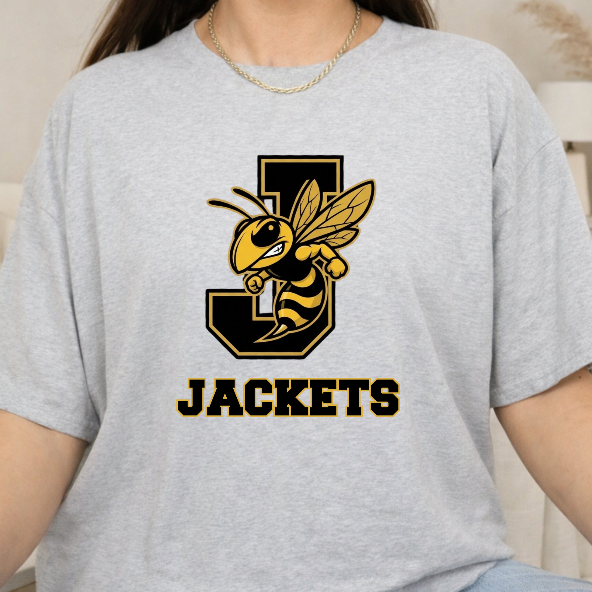 A person wearing a light heather gray short-sleeve T-shirt with a large black and yellow bee graphic over a stylized letter J and the word 'JACKETS' printed below.