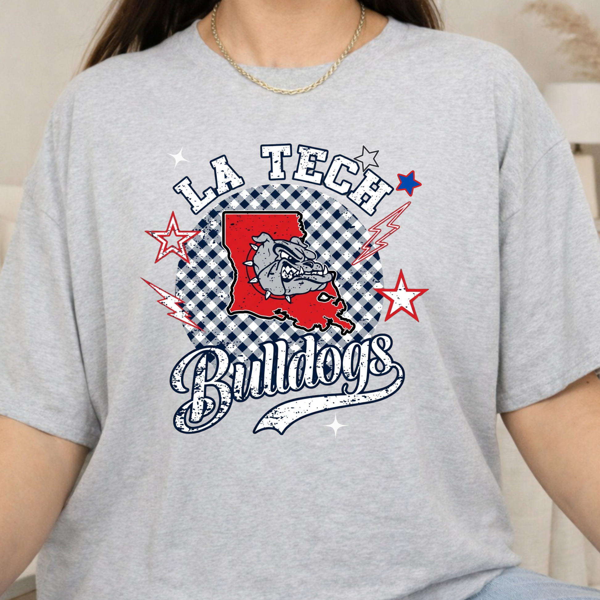 A person wearing a light heather gray graphic T-shirt with a red, white, and blue 'LA Tech Bulldogs' design on the front.