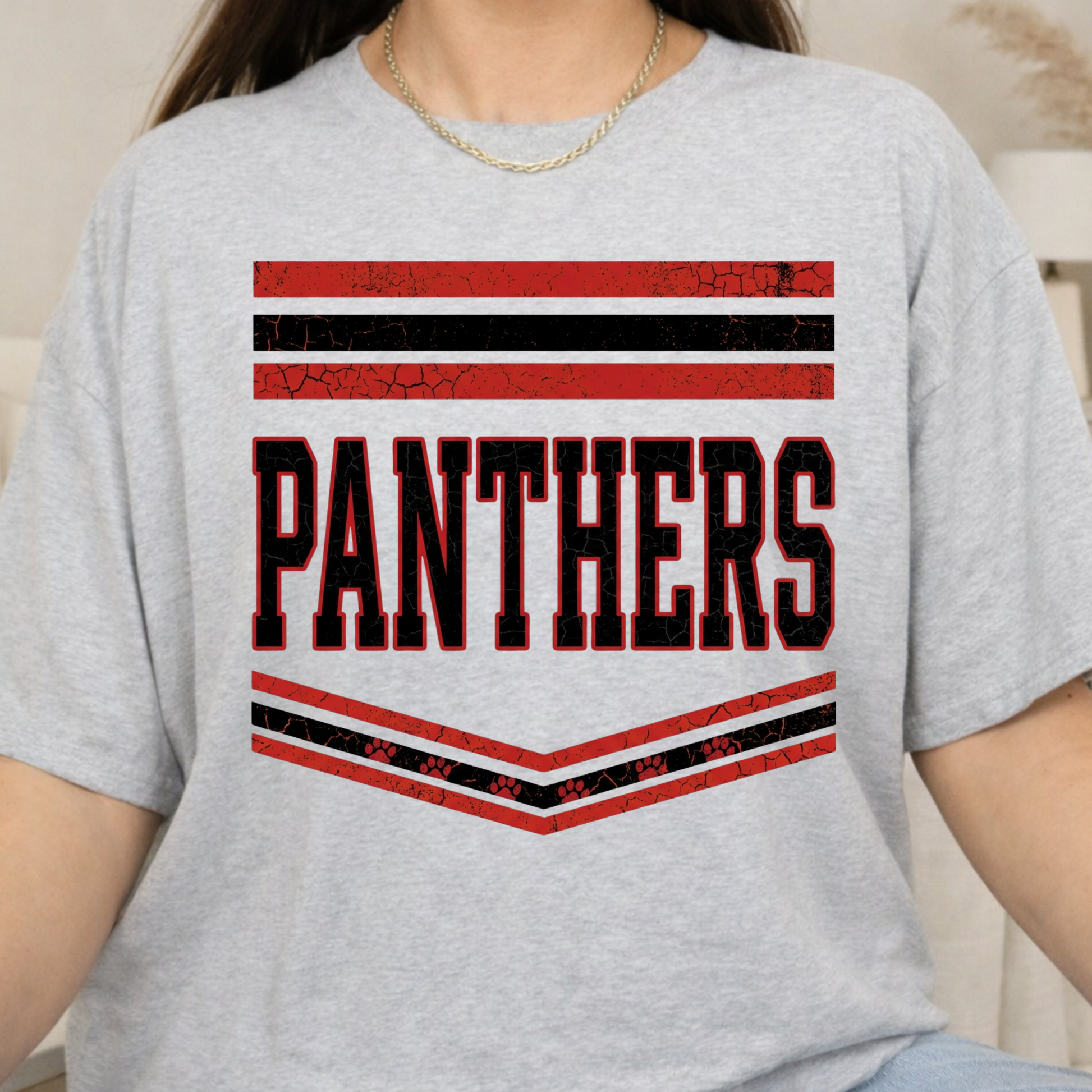A person wearing a light heather gray t-shirt with a distressed red and black 'PANTHERS' graphic on the chest.