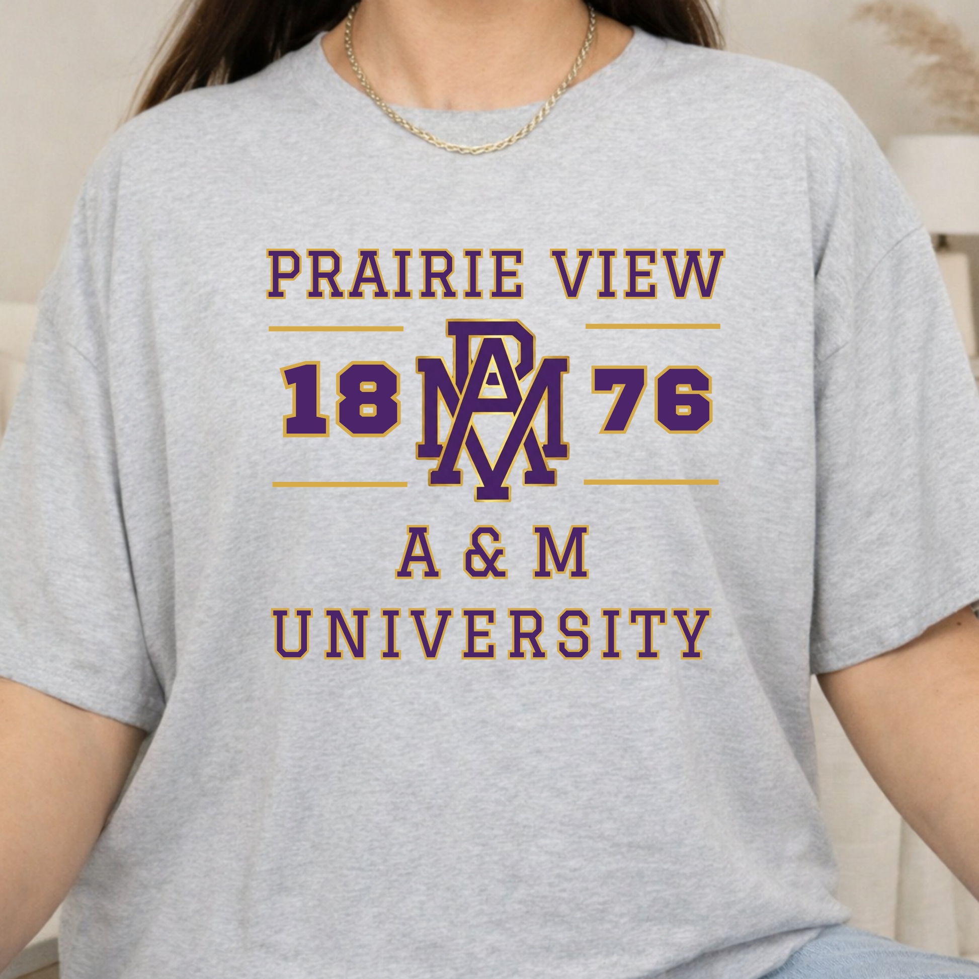 A person wearing a light heather gray graphic T-shirt with 'PRAIRIE VIEW 1876 A & M UNIVERSITY' printed in dark red and purple on the front.