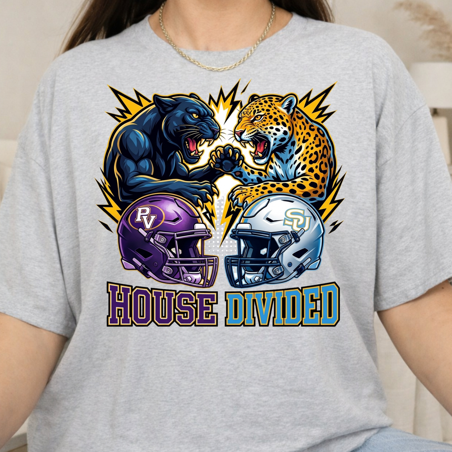 A person wearing a light heather gray graphic T-shirt. The shirt features a large football-themed graphic with a black panther and a leopard facing off, two helmets below them, and the words 'HOUSE DIVIDED' across the front.