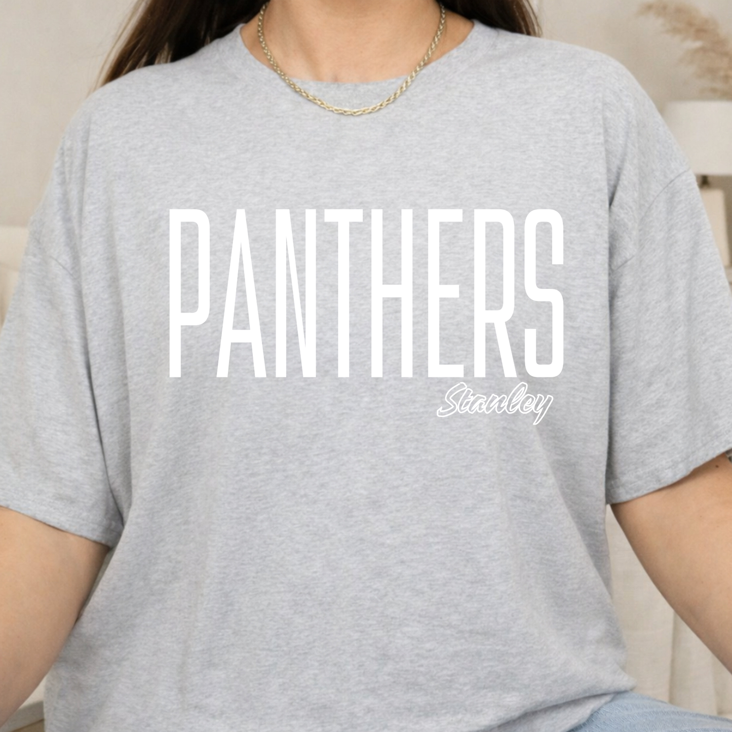 A person wearing a light heather gray short-sleeve T-shirt with large white 'PANTHERS' text and a smaller white 'Stanley' script logo on the front.