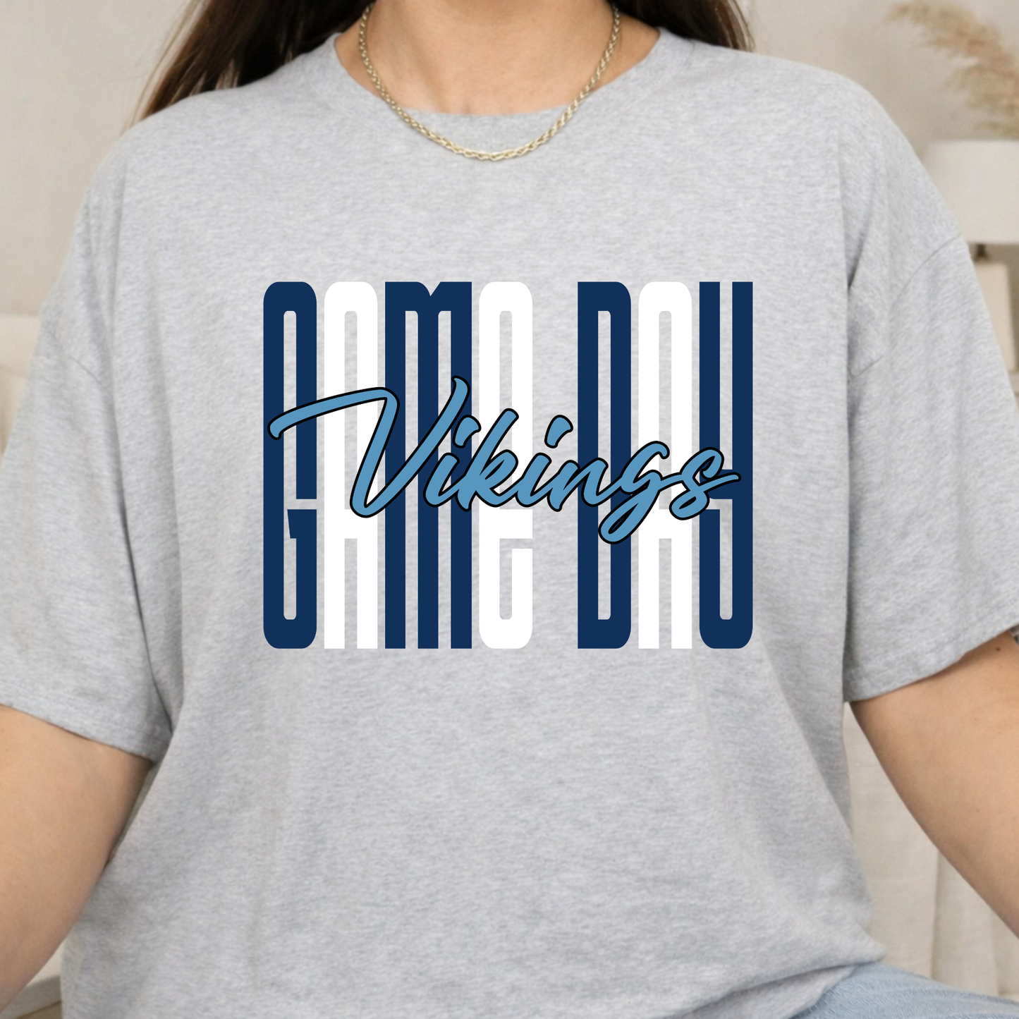 A person wearing a light heather gray t-shirt with a 'CAME DAY Vikings' graphic printed on the chest in navy blue and white.